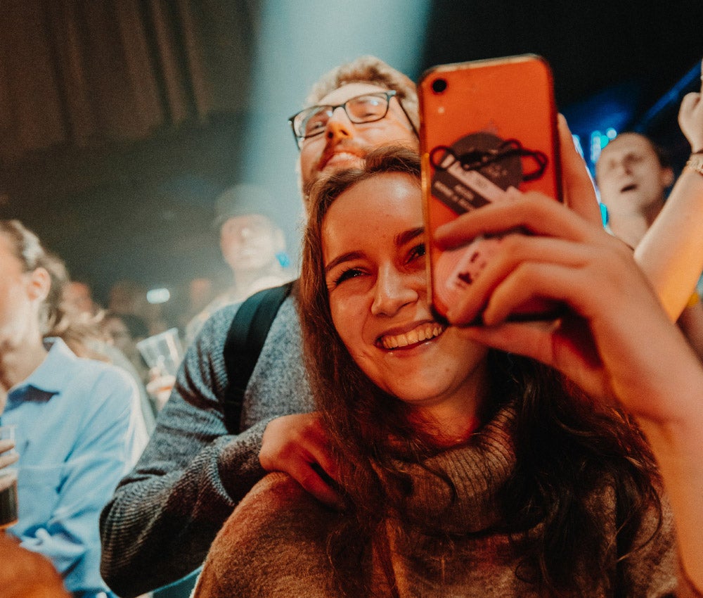 Photo of smiling people at an event, filming with a phone